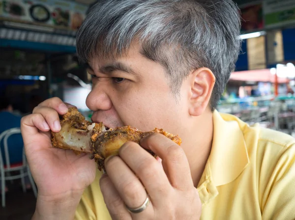 Asian man eating pork bone After eating the leg of crispy grilled pork knuckle. In the river restaurant in Thailand. He looks delicious and enjoys eating so much.