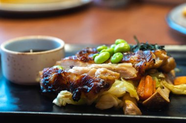 tavuk biftek sosu siyah plaka üzerinde fincan ile kapatın. Yeşil bezelye ve beyaz lahana, havuç ve restoranda mantarlı tavuk biftek üzerinde Japon deniz yosunu