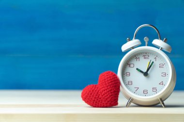 Sevgililer günü kavramı. El ahşap masa ve mavi arka plan üzerinde beyaz çalar saat önünde iplik kırmızı kalp yapmak