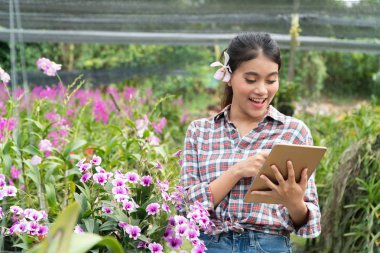 Kadın bahçıvanlar ekose gömlek giymek. Orkide kulak çekme, tablet tutarak ve tablete parmakları işaret ve ile gülümseyerek el sevinç.