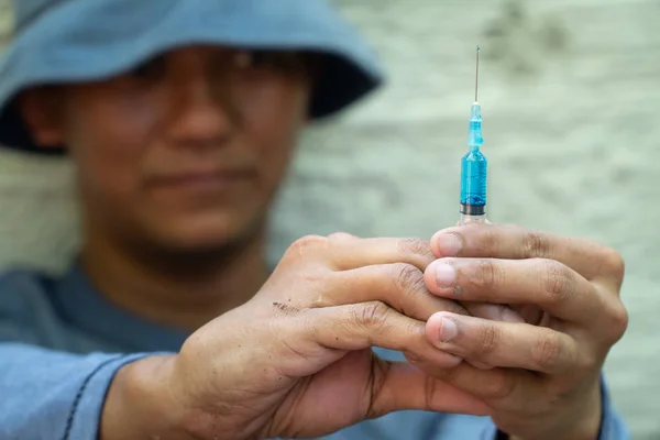 close up of Syringe and Needle in hand of drug addict man. homeless using needle injecting liquid. Drug concept and Danger of drugs