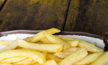 ahşap masa üzerinde kahverengi kenarlıklı beyaz bir tabak kızarmış patates kızartması