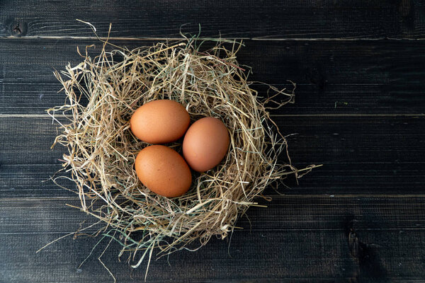 Fresh brown chicken eggs in hay nest on black wooden background. Concept of organic eggs, free space for text or other elements