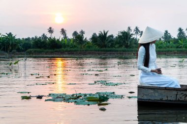 beyaz geleneksel Vietnam elbise (Ao Wai) ve Vietnam çiftçi şapkası giyen ve çiçek lotus gölünde ahşap tekne üzerinde oturan turist kadınlar. Gün batımının güzelliğini görmek için.