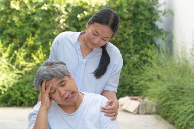 Felçli, bükülmüş ağızlı, el kıvrımlı ve zayıf uzuvları olan orta yaşlı ve obez erkekler tekerlekli sandalyede yorgun ve umutsuz hissediyorum ve bir eşin ona destek olmak için sevgi ve umutla ayakta durduğunu hissediyorum.
