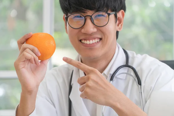 医師や栄養士はオレンジを保持し オレンジに指を向けます クリニックで笑顔 健康的な食事 健康のための処方箋としての栄養食品の概念 果物は薬です — ストック写真