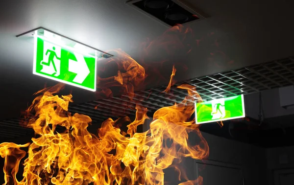 Green fire escape sign hang on the ceiling in the office at nigh