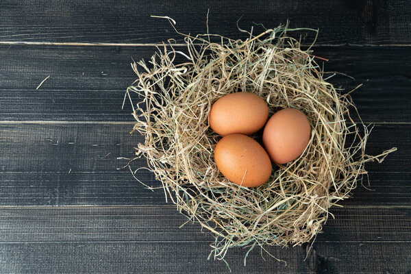 Fresh brown chicken eggs in hay nest on black wooden background. Concept of organic eggs, free space for text or other elements