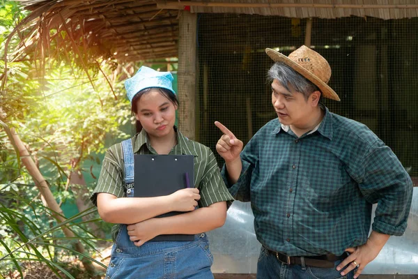 Couple farmers standing beside chicken farms. Women hold a clipboard and frustrated and sad gestures, Men are complaining After she made a mistake. Concept of Family farming.