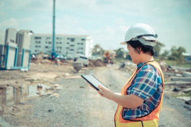 İnşaat yerinde ayakta tablet kullanarak baş kask ile Asya kadın inşaat mühendisi işçi portresi. arka planda Bina site yer. İnşaat konsepti