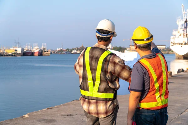 Two engineers stood wearing a safety helmet. Standing at the pier And holding the blueprint And consult the plan In the construction. Concept of efficient construction management.