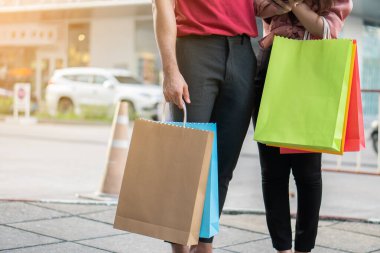 Alışveriş caddesinde yürüyen ve ellerinde renkli alışveriş torbaları tutan mutlu genç çiftler. Satış ve Kara Cuma alışverişi kavramı