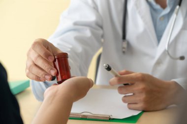 Steteskoplu ve üniformalı bir Asyalı doktor elinde ilaç şişesiyle hastaların tıbbi özelliklerini açıklıyor. Tıbbi danışmanlık ve tıbbi hizmetler kavramı