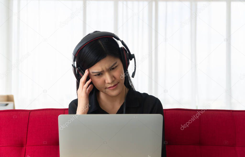 Unhappy Asian woman sitting on a sofa and video conference with a business partner on a laptop, Her so are Bored and headache. Concept of a new lifestyle and social distancing