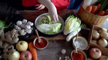 Geleneksel Kore kıyafetleri giyen Asyalı kadınlar, sarımsak, gochugaru (Kore biberi) ve taze sebze gibi malzemelerle el yapımı tuz ve Kimchi malzemeleri serpiyorlar..