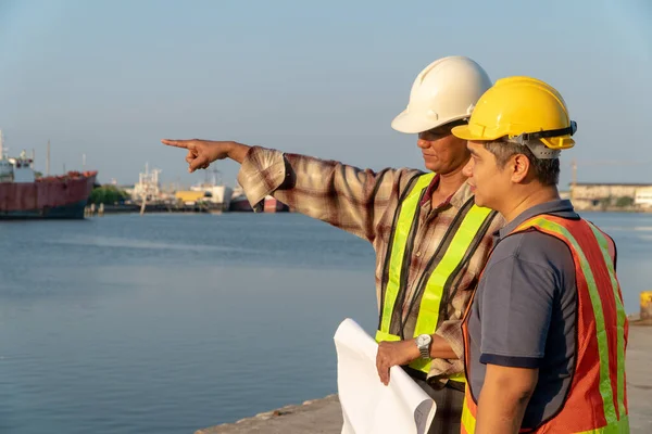 Two engineers stood wearing a safety helmet. Standing at the pier And holding the blueprint And consult the plan In the construction. Concept of efficient construction management.