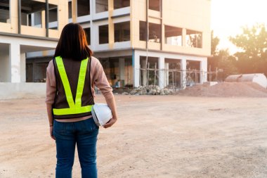 İnşaat alanında dikilirken miğfer takan Asyalı bir mühendis kadının portresi. Arkaplanda inşa yeri, Eşitlik ve başarı kavramı