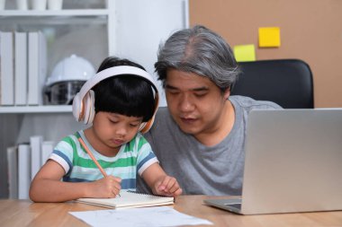 Asyalı baba evde kızıyla birlikte çalışıyor ve okuldan online öğrenim görüyor. Karantina sırasında yeni yaşam tarzı normal. Evde kalma kavramı, serbest çalışma ve babalık kavramı