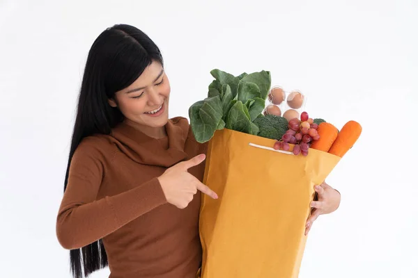 幸せなアジアの女性は笑顔で指を紙袋に向け 食料品からの宅配便が自宅で配達された後に買い物袋を運びます 新しいライフスタイルのためのスーパーマーケットデリバリーの概念 — ストック写真