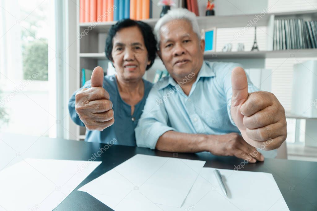 Senior Asian couple using the calculator and paperwork on desk at home to calculate expenses and income. And savings after retirement. Concept of financial planning and investment for retirees.
