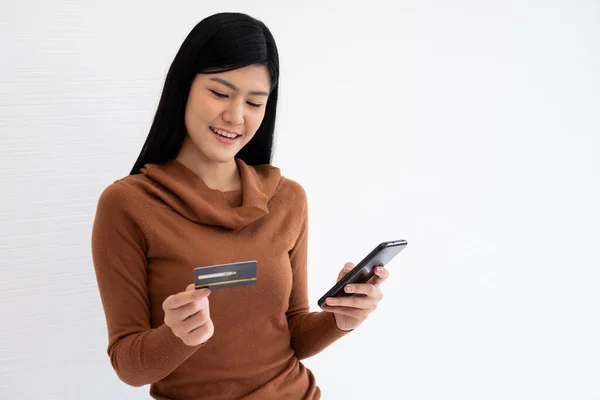 Happy Asian woman holding card credit and smartphone for mobile banking on the internet. Concept of new lifestyle and financing technology.
