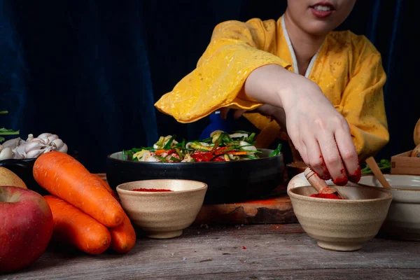 Asian women wearing Korean traditional costumes (hanbok) are mixing fresh stir-fry and kimchi ingredients with ingredients such as salt, garlic, gochugaru, fresh vegetables. — Stock Image Asian Women Wearing Korean Traditional Costumes Hanbok Mixing Fresh Stir Stock Photo