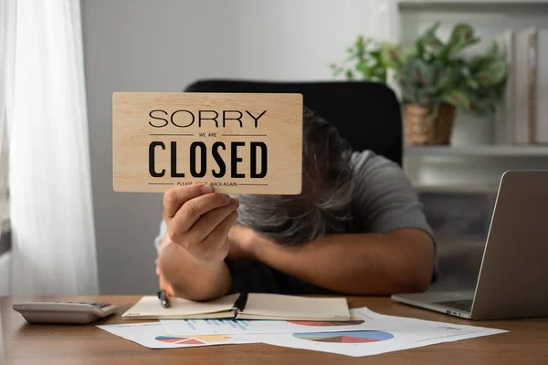 The owner of the business is stressed and disappointed. And holding a sign to close the business after the revenue and cost was raised and recognized the loss