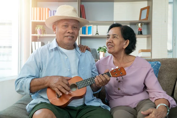 Happy Asian senior couple playing ukulele and singing together at home. The concept of life for the elderly after happy retirement