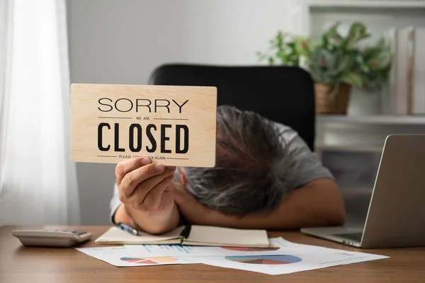 The owner of the business is stressed and disappointed. And holding a sign to close the business after the revenue and cost was raised and recognized the loss