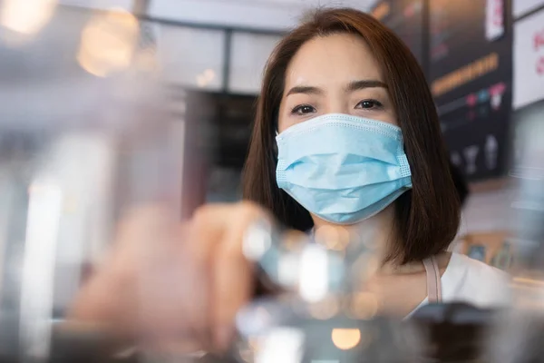 コーヒーカップと伝染病を防ぐためにフェイスマスクを着用し コーヒーショップで顧客にサービスを提供するアジアのバリスタ女性の背景の選択的な焦点 Covid 19からの予防の概念 — ストック写真