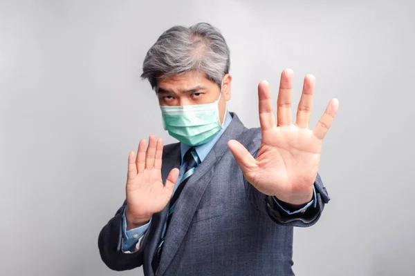 Selective focus of hand. Portrait of Asian businessman with surgical medical mask looking at camera and Raise your hand to forbid. Concept of preventing contagious diseases COVID 19