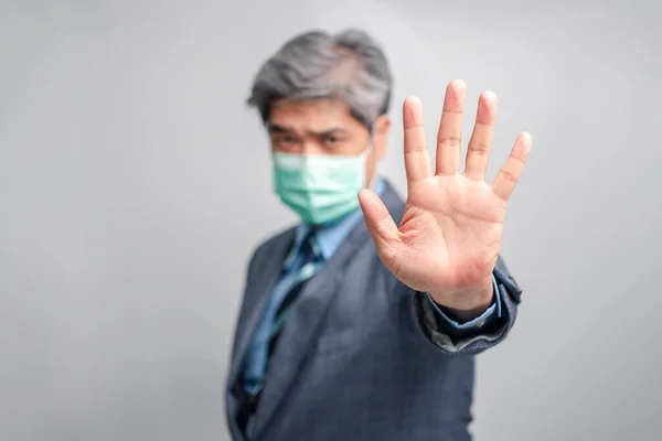 Selective focus of hand. Portrait of Asian businessman with surgical medical mask looking at camera and Raise your hand to forbid. Concept of preventing contagious diseases COVID 19