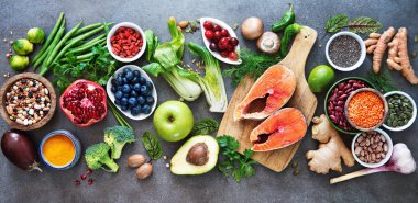 Healthy food selection: food sources of omega 3 and unsaturated fats, fruits, vegetables, seeds, superfoods with high vitamin e and dietary fiber, cereals on gray background