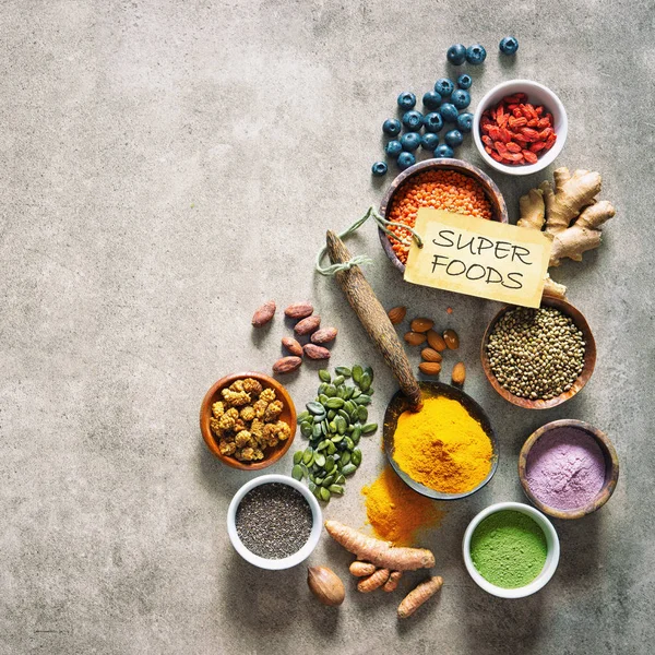 Various colorful superfoods as acai powder, turmeric, matcha green tea, quinoa, pumpkin seeds, blueberry, dried goji berries, cape gooseberries, raw cocoa, hemp seeds and other in bowls