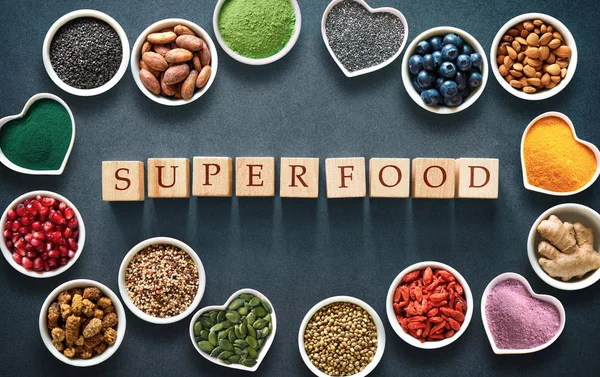 Various colorful superfoods as acai powder, turmeric, matcha green tea, spirulina, quinoa, pumpkin seeds, blueberry, dried goji berries, cape gooseberries, raw cocoa, hemp seeds and other in bowls on dark background