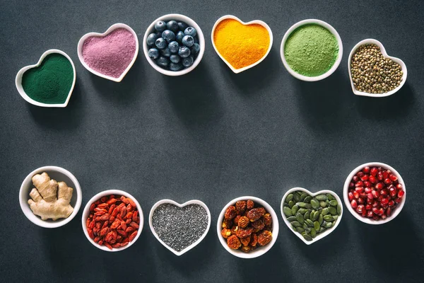 Various colorful superfoods as acai powder, turmeric, matcha green tea, spirulina, quinoa, pumpkin seeds, blueberry, dried goji berries, cape gooseberries, raw cocoa, hemp seeds and other in bowls on dark background