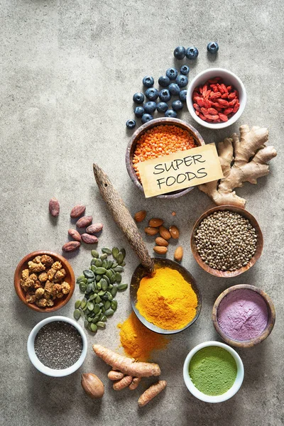 Various colorful superfoods as acai powder, turmeric, matcha green tea, quinoa, pumpkin seeds, blueberry, dried goji berries, cape gooseberries, raw cocoa, hemp seeds and other in bowls