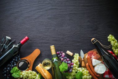 Üzüm, peynir, jambon ve mantar kopya alanı ile koyu arka plan üzerinde şarap şişeleri