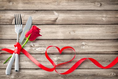 Silverware tied up with red ribbon in heart shape on wooden planks. Concept Valentines Day dinner. Restaurant party celebration clipart