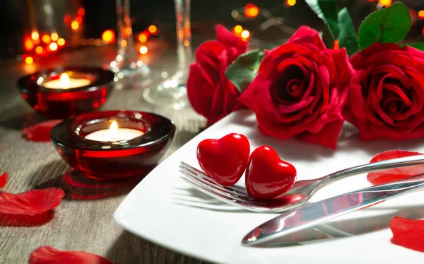 Festive table place setting for Valentines day dinner with red roses and burning candles