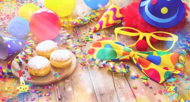 Colorful carnival or party background with donuts, balloons, streamers and confetti and funny face formed from wig, nose and glasses on rustic wooden planks with copy space clipart