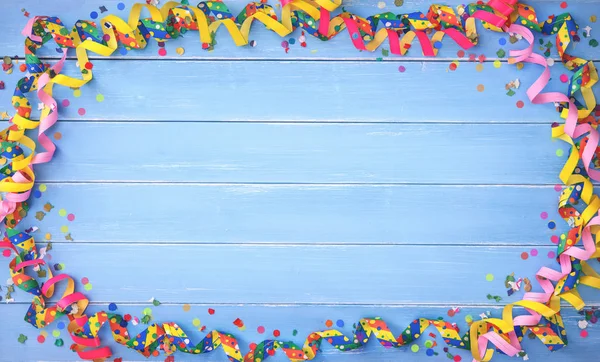 Colorful carnival or birthday background with streamers and confetti on blue wooden planks