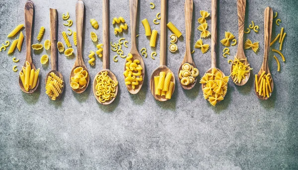 Varios tipos de pasta en cucharas de madera sobre fondo de piedra —  Fotos de Stock