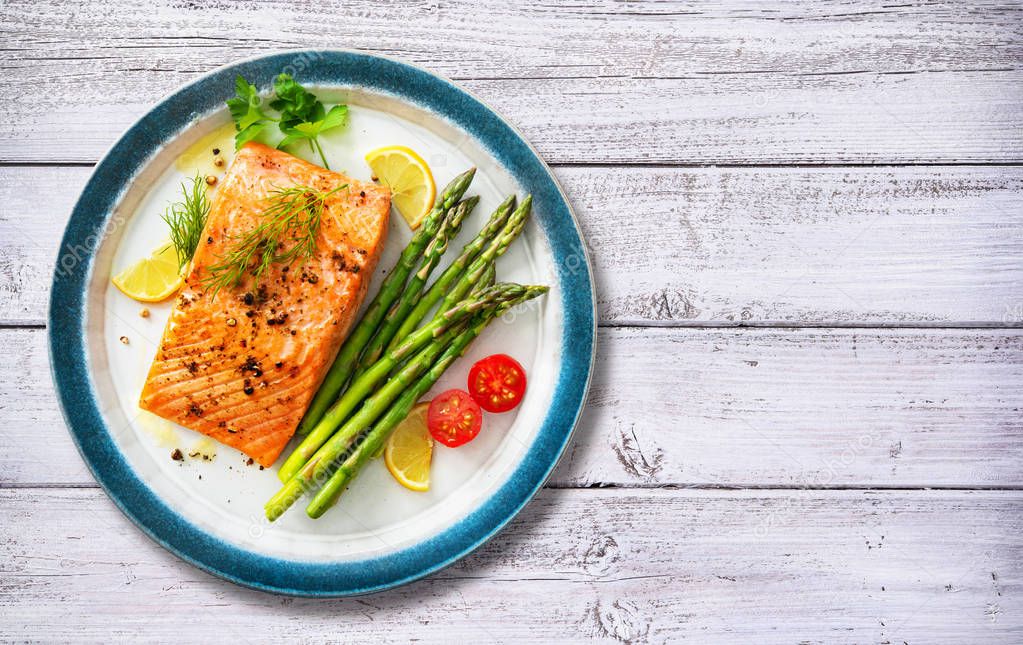 Grilled salmon steak garnished with green asparagus, lemon and t