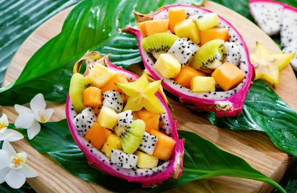 Ensalada de frutas exóticas servida en media fruta de dragón sobre hojas de palma —  Fotos de Stock