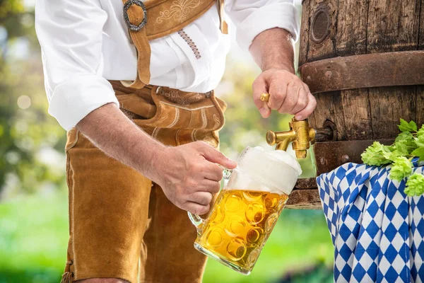 Bavarian man in leather trousers is pouring a large lager beer — Stock Photo, Image