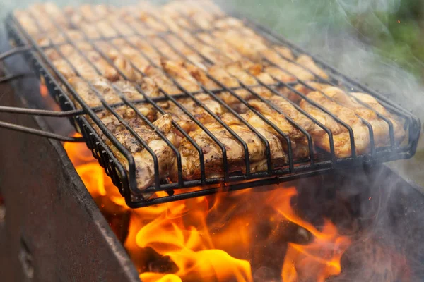 Grillezett csirke a grillen. Feldolgozásfőzés csirkelábak egy barbecue grill szabadban lángok és füst a háttérben. — Stock Fotó