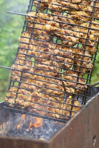 Frango grelhado no grelhador. Processando pernas de frango em um churrasco grill ao ar livrechamas e fumaça no fundo. — Fotografia de Stock