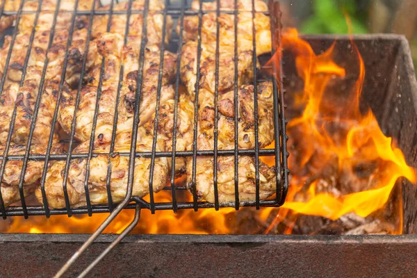 Frango grelhado no grelhador. Processando pernas de frango em um churrasco grill ao ar livrechamas e fumaça no fundo. — Fotografia de Stock
