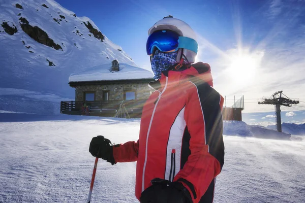 young boy on ski slope with goggles and reflection of snowed mountains on the mask. Portrait of skier at the ski resort with mountain shelter and snow on background